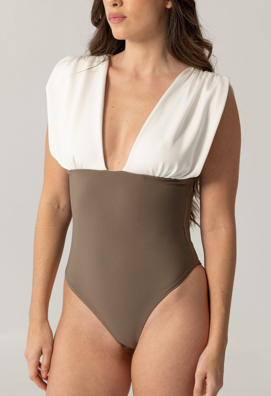 Woman wearing ARIEL one-piece swimsuit with deep V neckline and wide white shoulder detail paired with taupe fitted bottom, luxury swimwear for modest women.