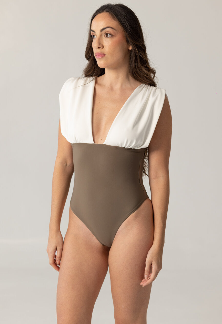 Woman wearing ARIEL one-piece swimsuit with deep V neckline and contrasting white shoulder detail against neutral background
