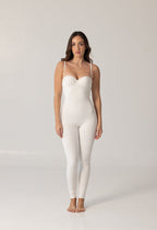 Woman wearing a sleek white fitted bodysuit with thin straps, standing barefoot against a neutral background showcasing the elegant NURA BODY design.