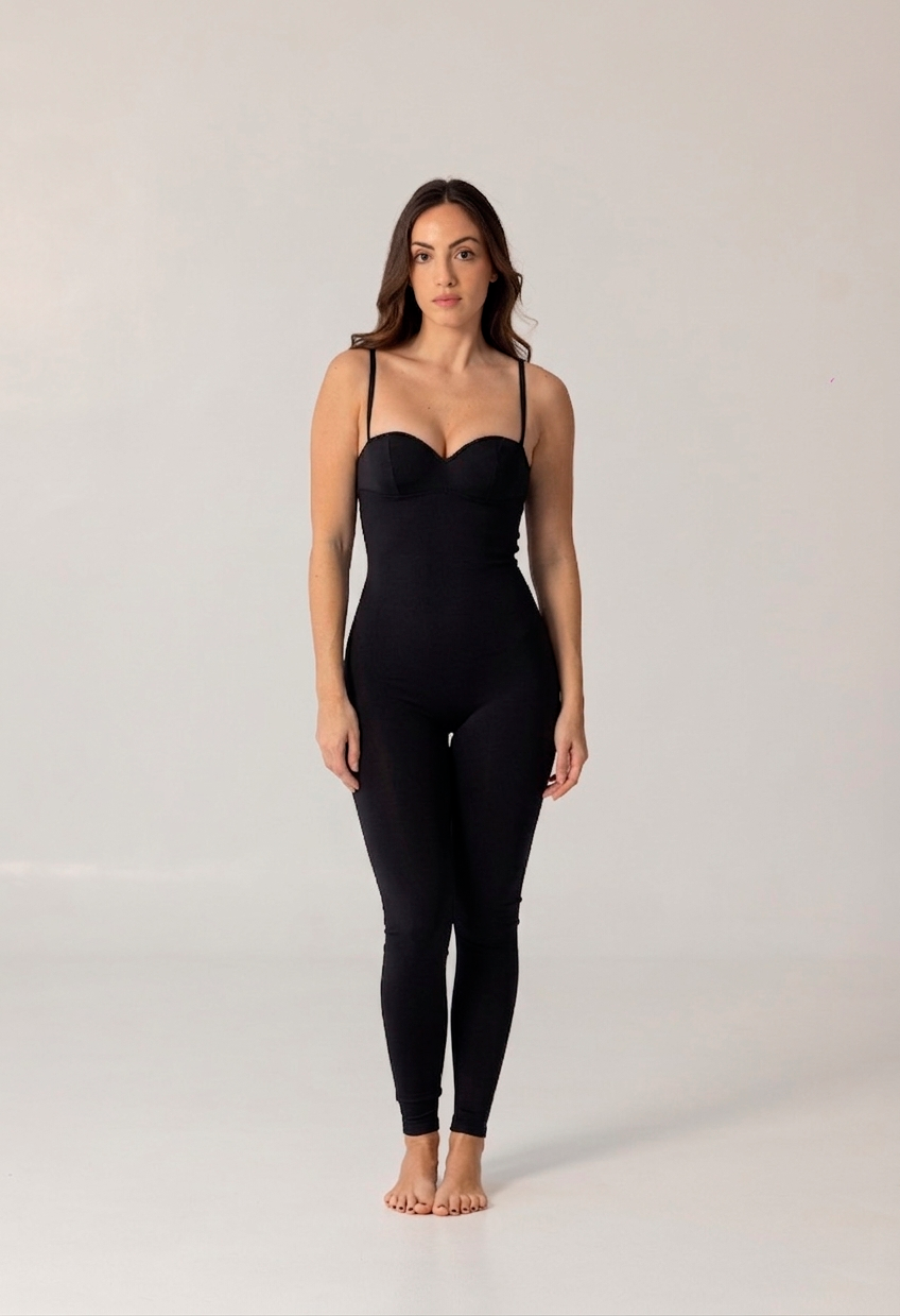 Woman wearing a sleek, black fitted jumpsuit with thin straps, showcasing the elegant and modern style of NURA BODY luxury swimwear.