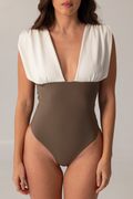 Woman wearing ARIEL luxury swimwear one-piece swimsuit with deep V-neck and structured white shoulder detail, in neutral tones suitable for resort wear.